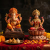 Handcrafted Ganesha and Lakshmi murtis seated side by side on a puja pedestal with diyas and marigolds