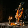 Handcrafted Krishna murti playing the flute in a mandir niche with a peacock feather and diya