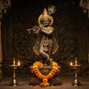 Krishna murti with peacock feather crown and flute in a mandir niche with marigold garland and diyas